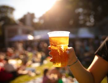 person, out of frame, holding a glass of light beer at an outdoor festival
