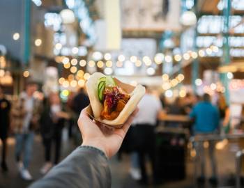man holding up a bao bun in an outdoor area with a blurry background