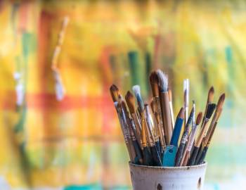 paint brushes in a cup with large canvas in background